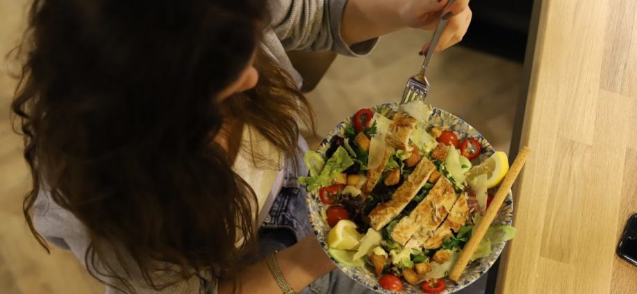 Overhead view of a woman eating a chicken salad balancing health with deliciousness.
