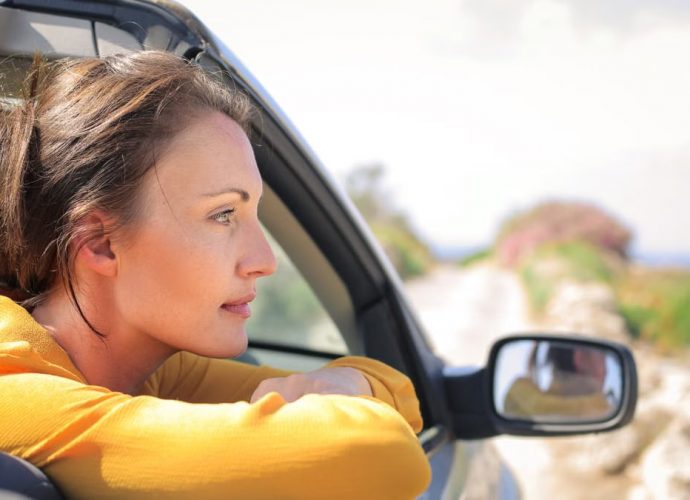 Profile view of a woman leaning out a convertible car enjoying a sunny day on a scenic road.